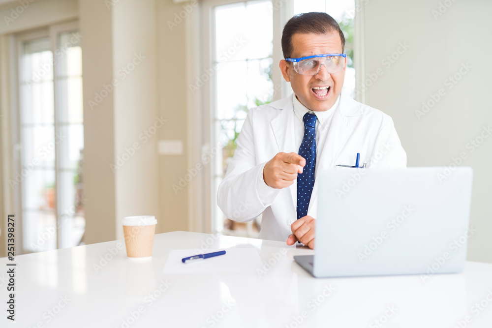 Middle age scientist man wearing professional glasses working using laptop very happy pointing with hand and finger Middle age scientist man wearing professional glasses working using laptop very happy pointing with hand and finger