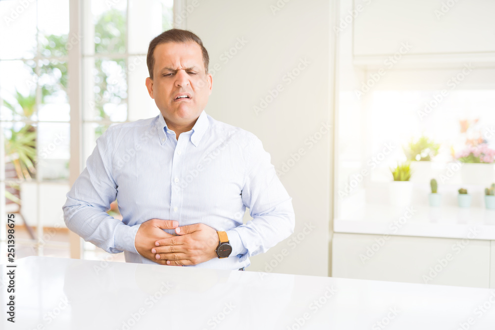 Middle age man sitting at home with hand on stomach because indigestion, painful illness feeling unwell. Ache concept. Middle age man sitting at home with hand on stomach because indigestion, painful illness feeling unwell. Ache concept.