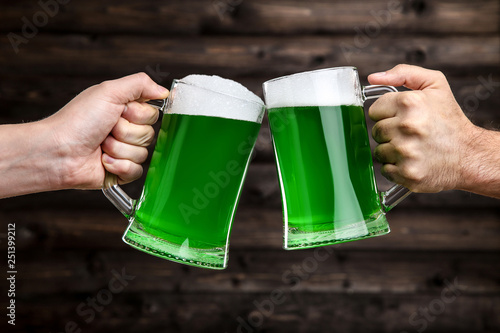St. Patrick's Day. Glass mugs with green beer in male hands on wooden background