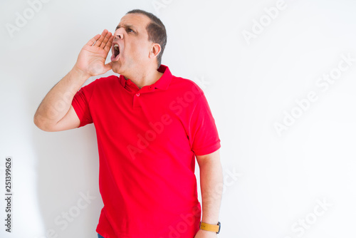 Middle age man wearing red t-shirt over white wall shouting and screaming loud to side with hand on mouth. Communication concept.