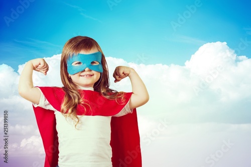 Portrait of  beautiful little girl in superhero costume on sky background