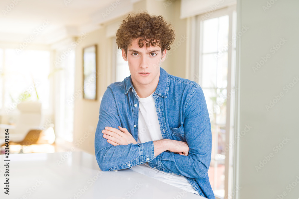 Young handsome man wearing casual denim jacket at home skeptic and nervous, disapproving expression on face with crossed arms. Negative person.