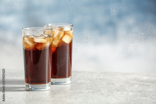 Glasses of cold cola on table against color background. Space for text