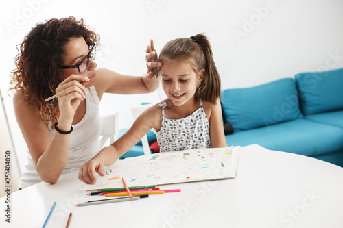 Mother teach her daughter to draw.They sitting at the table in living room.