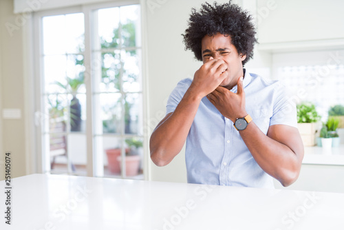 African American business man smelling something stinky and disgusting, intolerable smell, holding breath with fingers on nose. Bad smells concept.