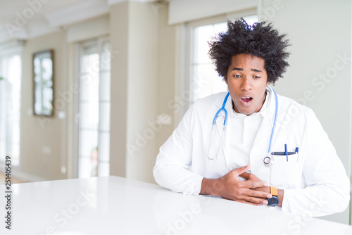 African American doctor man at the clinic with hand on stomach because indigestion, painful illness feeling unwell. Ache concept.