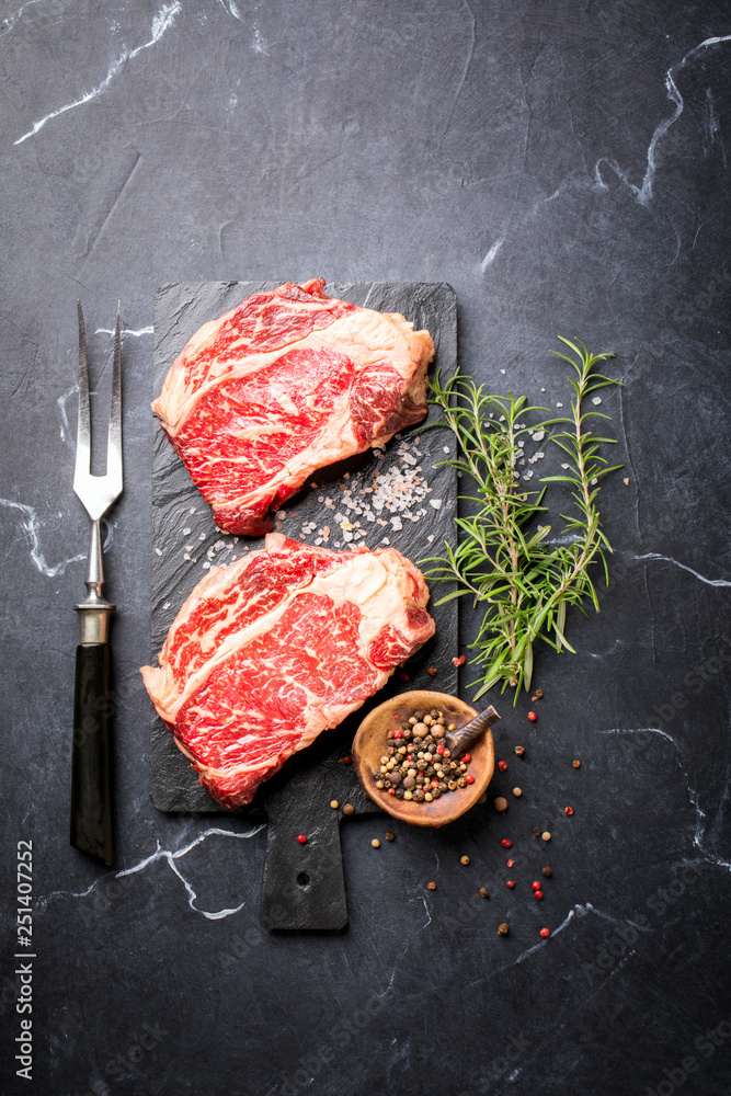 Raw Fresh Marbled Meat Beef Steak rosemary, spices slate on board. Black marble background. Top View Copy space for Text