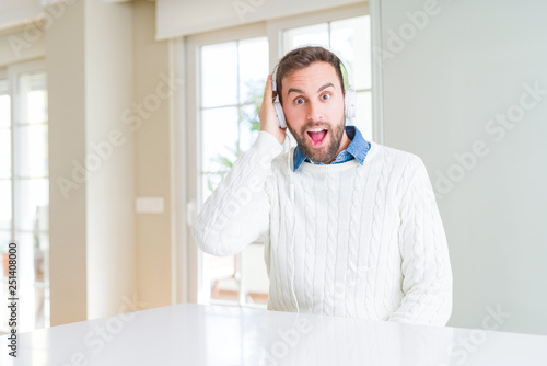 Handsome man wearing headphones and listening to music scared in shock with a surprise face, afraid and excited with fear expression