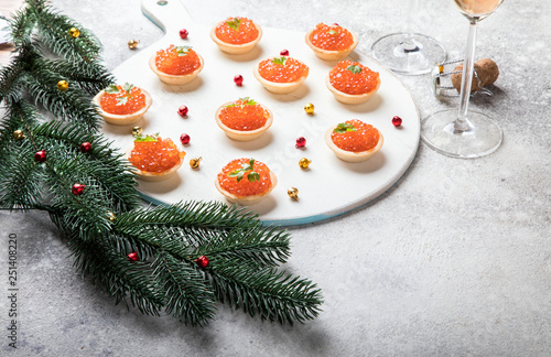 Christmas and New Year holidays composition. Red Salmon Caviar in Tartlets. Festive Appetizer and champagne on gray background.Copy space for Text.