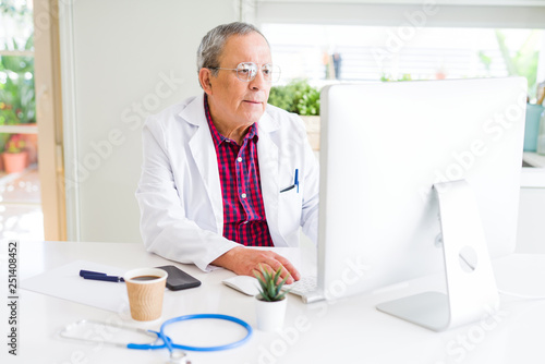 Handsome senior doctor man doing research using laptop looking for a cure at the clinic with a confident expression on smart face thinking serious
