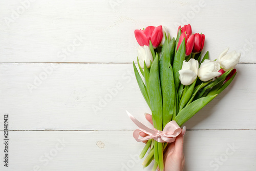 Womans hand holding Bouquet of tulips on white wooden horizontal striped board. Greeting card for International Womans Day, Mothers Day, wedding, birthday, spring holidays. Vintage mockup, copy space