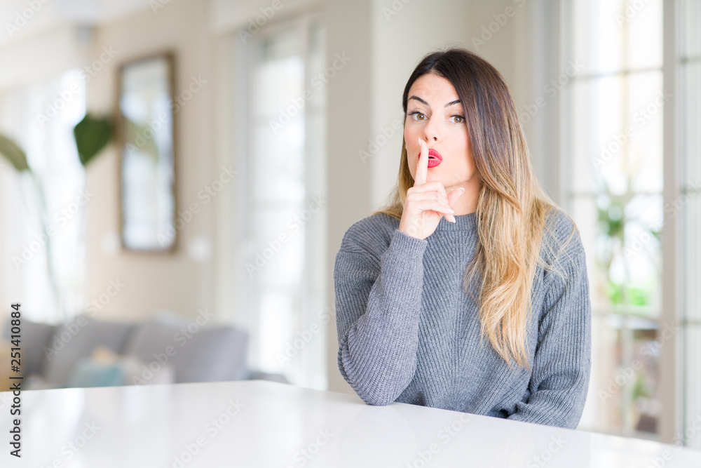 Young beautiful woman wearing winter sweater at home asking to be quiet with finger on lips. Silence and secret concept. Young beautiful woman wearing winter sweater at home asking to be quiet with finger on lips. Silence and secret concept.