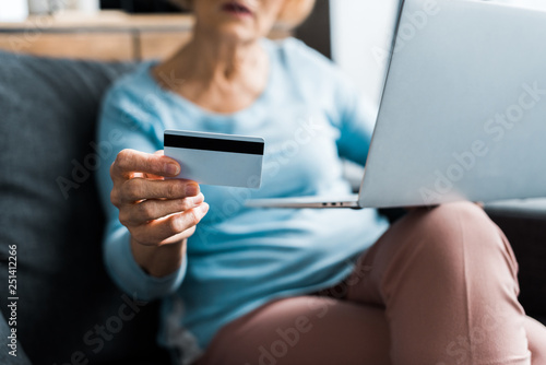 cropped view of senior woman sitting, holding credit card and using laptop while doing online shopping at home © LIGHTFIELD STUDIOS