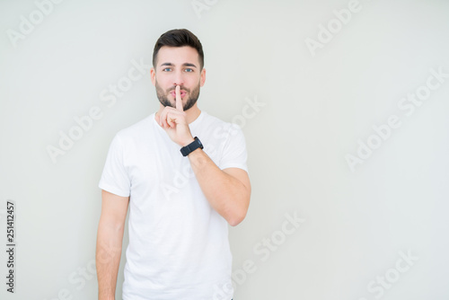 Young handsome man wearing casual white t-shirt over isolated background asking to be quiet with finger on lips. Silence and secret concept.