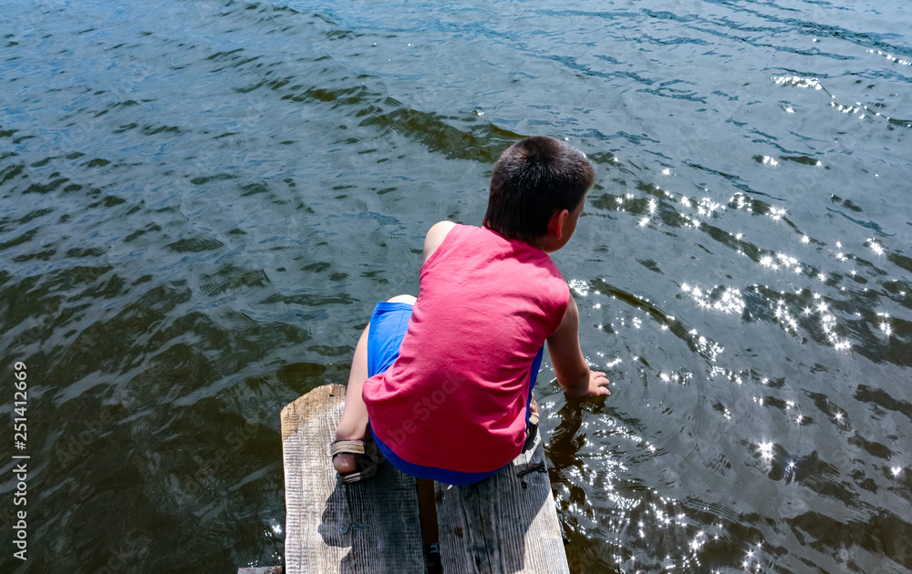 boy playing with water sitting on a wooden bridge on the shore of the lake, view from above boy playing with water sitting on a wooden bridge on the shore of the lake, view from above