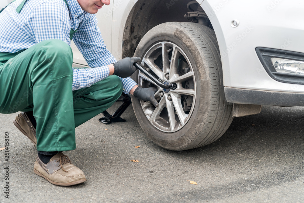 Naklejka premium Man fixing wheel in car on roadside