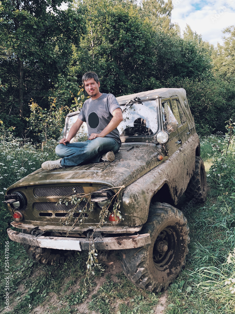 Fototapeta premium Young man sitting on a hood of off-road trophy car 4x4