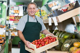 Positive man employee showing box with natural tomatos