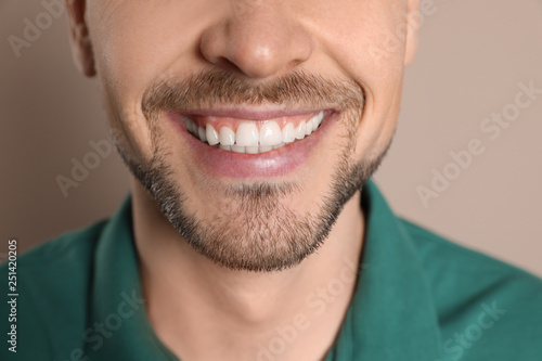 Smiling man with perfect teeth on color background, closeup