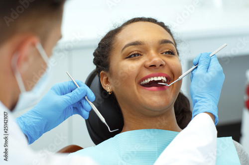Woman sitting on dental chair  smiling while dentist cures her teeth.