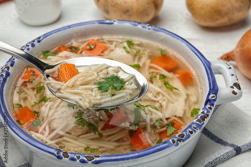 Spoon with fresh homemade chicken soup over dish, closeup