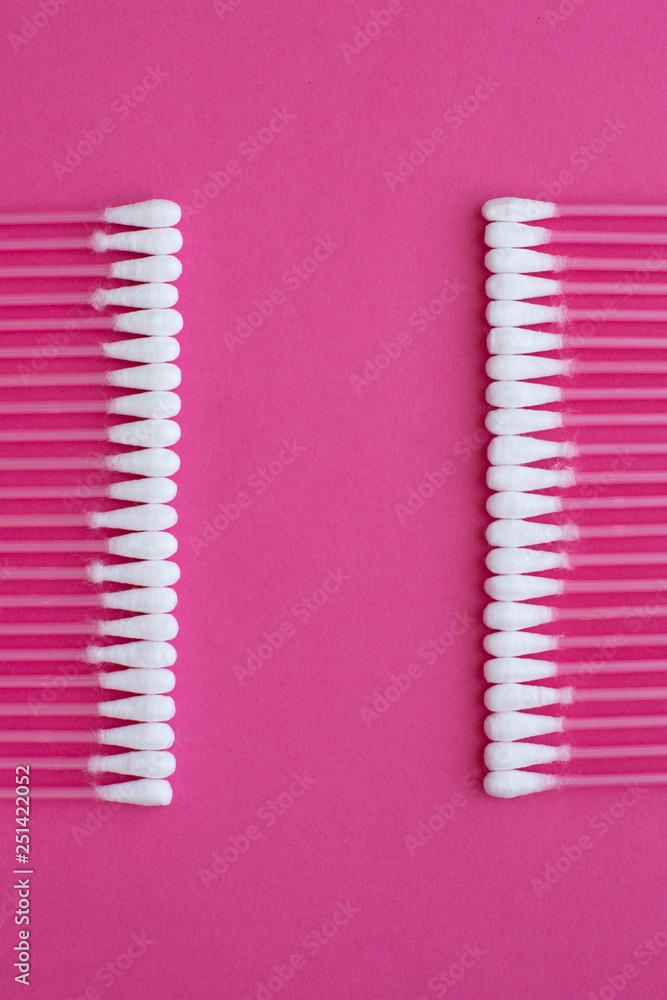 Closeup top view on cotton buds laid in a two vertical line on pink background Closeup top view on cotton buds laid in a two vertical line on pink background