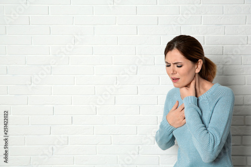 Woman suffering from cough near brick wall. Space for text