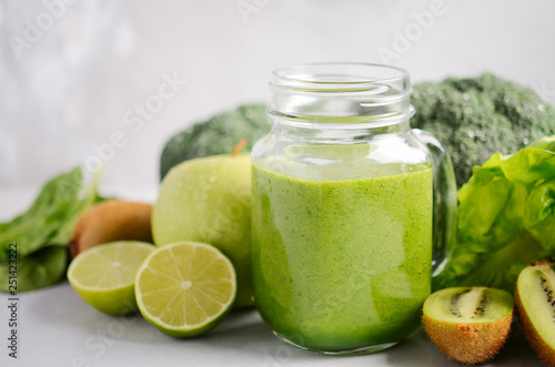 Fresh green smoothie in a jar with ingredients on a gray concrete background, selective focus.
