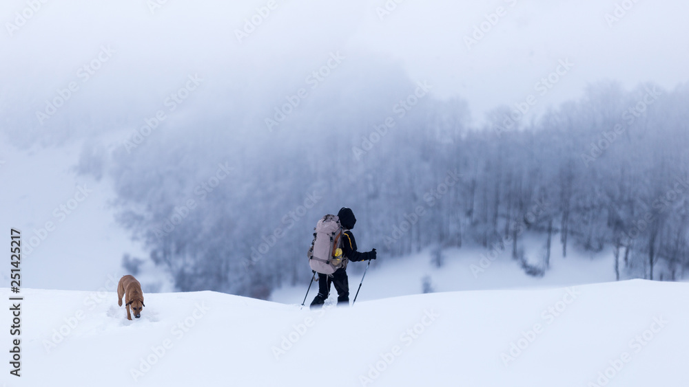Young man trekking together with his dog through a cold winter day in the mountains of Romania Young man trekking together with his dog through a cold winter day in the mountains of Romania