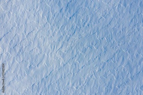 Aerial view of snow covered ground texture with rough wavy surface created by wind. Abstract winter background in blue tone