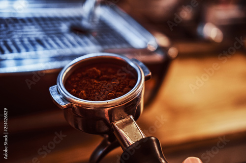 Close-up photo of a barista hand holding a portafilter with a black ground coffee in a cafe shop or restaurant