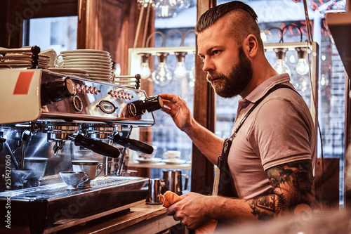 Handsome barista in uniform preparing a cup of coffee for a customer in the coffee shop