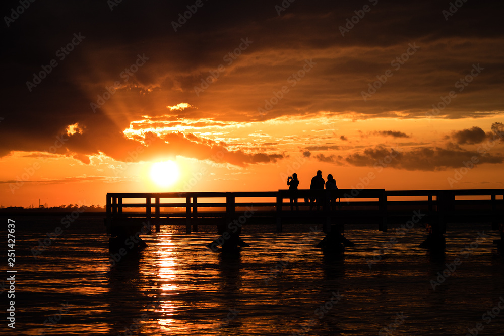 Silhouette of young adults on a fishing pier watching the sunset. Hanging out with friends, enjoying nature. Long Island New York.  