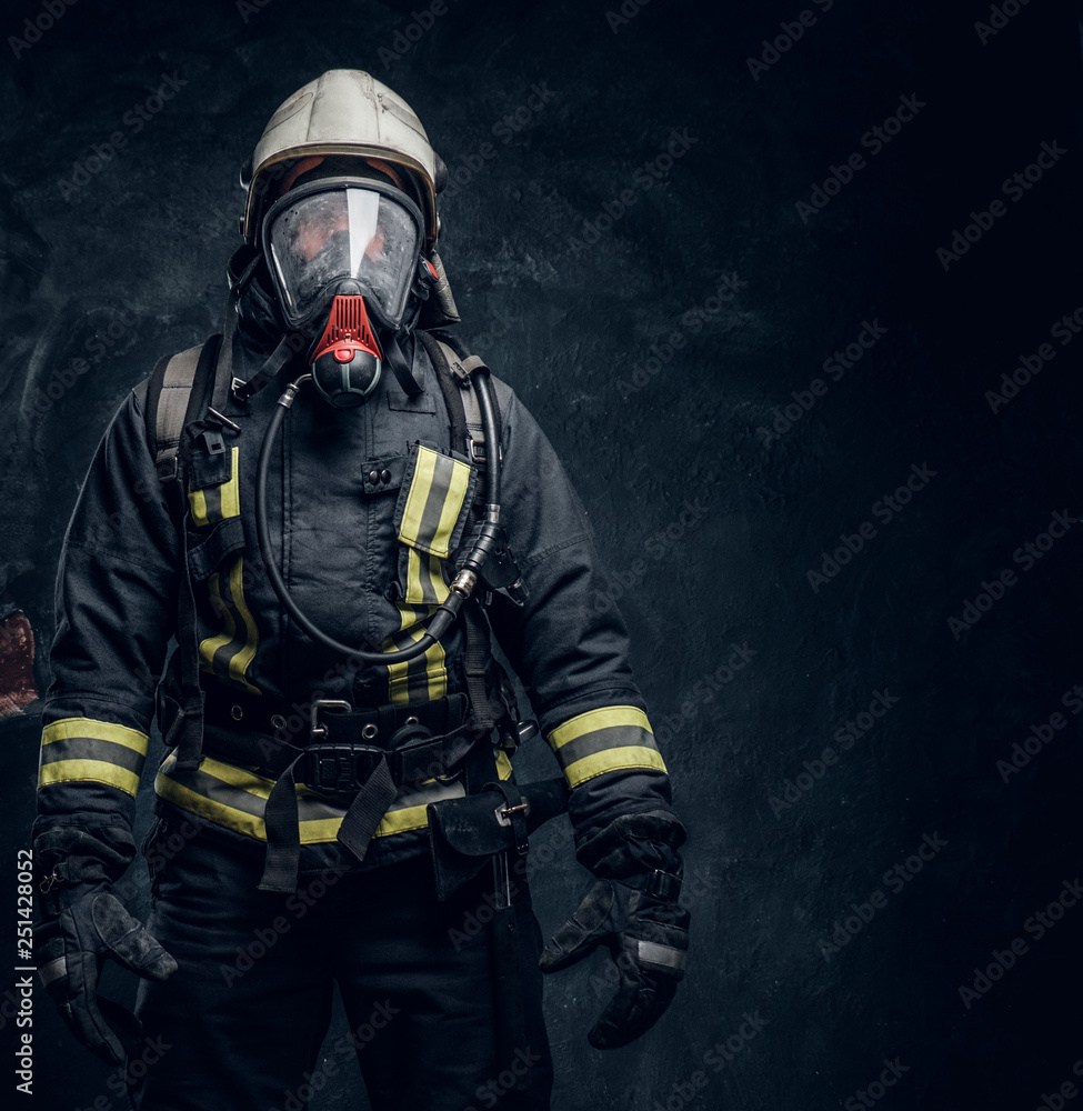 Obraz premium Firefighter in safety helmet and oxygen mask wearing protective clothes. Studio photo against a dark textured wall
