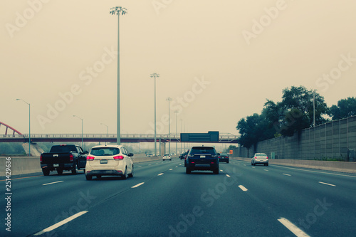 Traffic on highway in fog mist. Cars on freeway road at evening in american city country. Poor visibility in bad weather conditions. Toned with retro vintage film hipster filters.