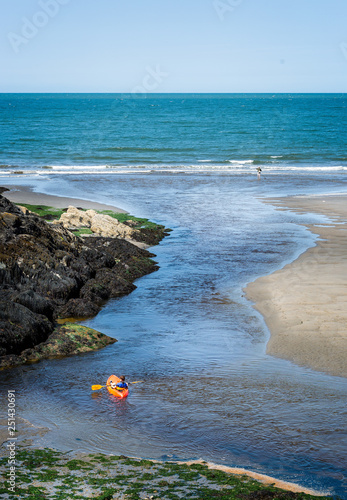 Boy paddling orange kayak in tidal inlet leading to the sea