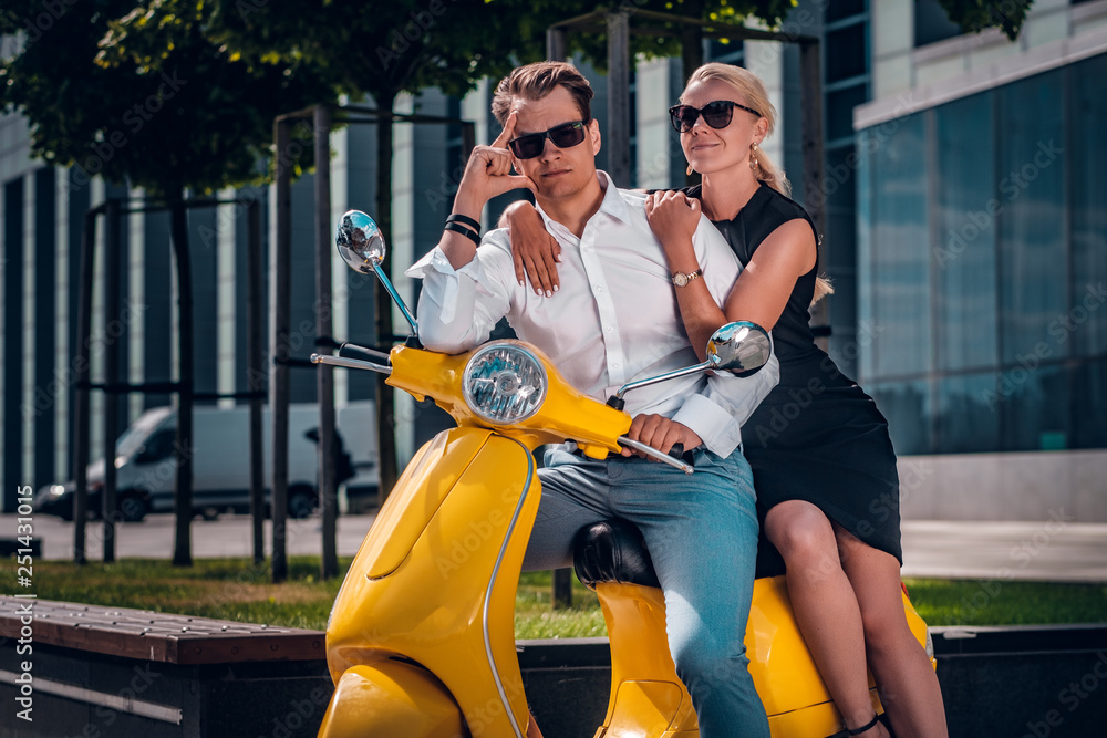 Beautiful romantic couple sitting on a classic Italian scooter on the street of a modern part of a European city