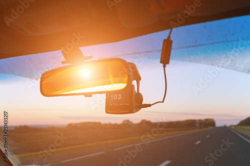 Front seat view of road, rear view mirror and speed recorder in sunlight. Blurred motion
