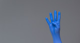 hand in surgical glove shows four fingers on neutral background. Copy space.
