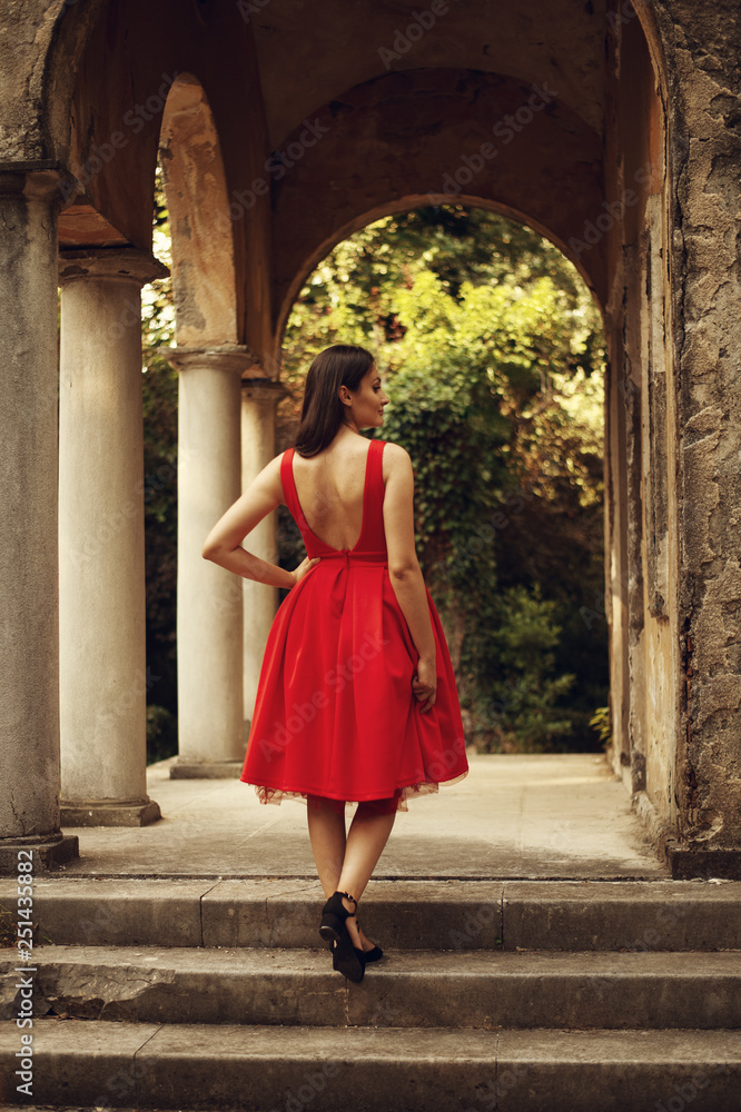 Portrait of beautiful woman wearing red classy dress. View from behind.