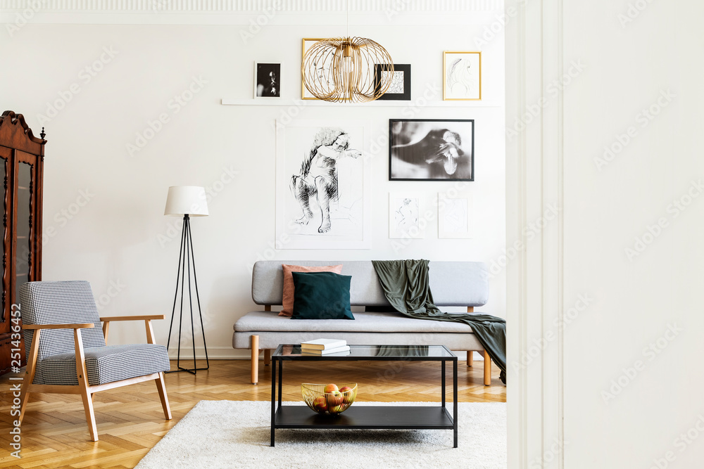 Obraz premium Table on carpet next to armchair in living room interior with posters above grey couch. Real photo