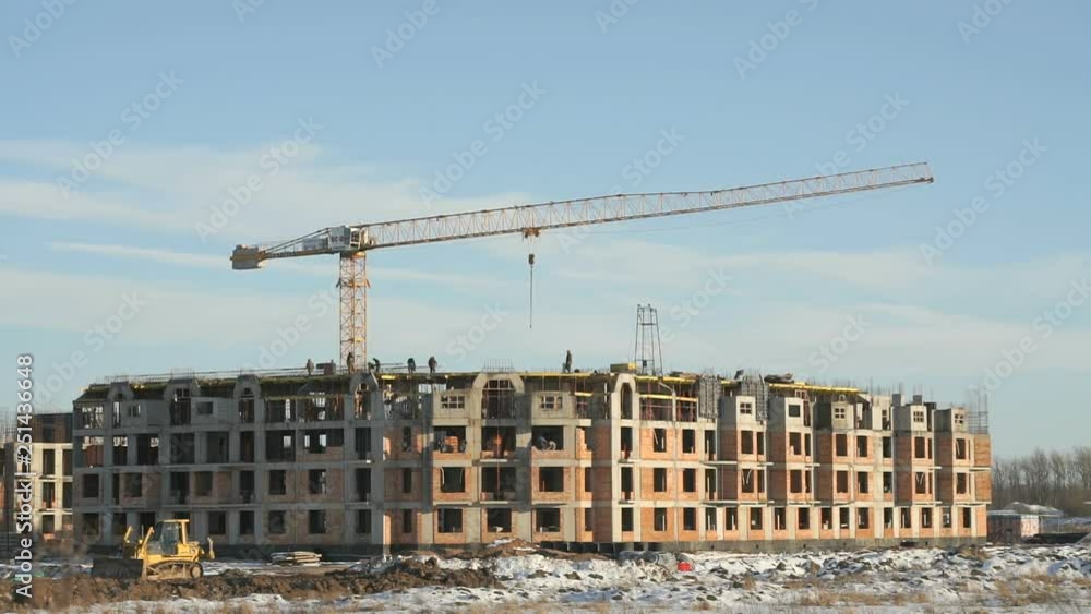 Construction of an apartment building. Builders work on the construction site. Construction crane works on the background the blue sky in winter Construction of an apartment building. Builders work on the construction site. Construction crane works on the background the blue sky in winter