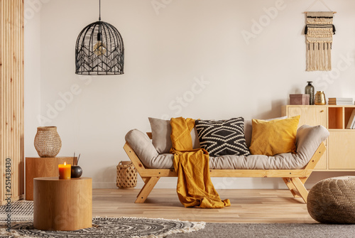 Scandinavian sofa with pillows and dark yellow blanket in bright living room interior with black chandelier photo