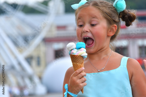 cute girl in a beautiful dress eating cone with multi-colored marshmallows