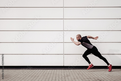 Side view of fit, sports man running by the wall with copy space