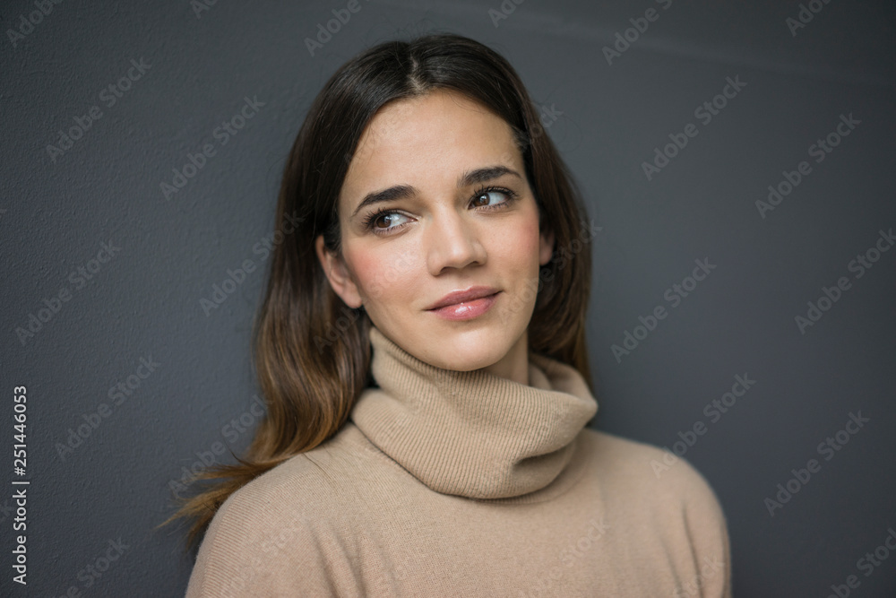 Portrait of smiling woman wearing light brown turtleneck pullover against grey background Portrait of smiling woman wearing light brown turtleneck pullover against grey background
