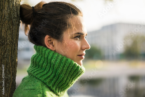 Profile of relaxed woman wearing green turtleneck pullover leaning against tree trunk
