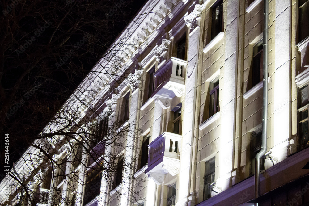 The facade of old building with columns is at night lighted up by decorative lanterns..
