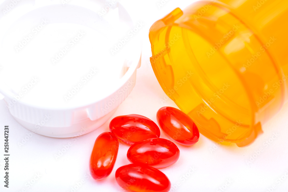 Fototapeta premium Docusate sodium soft gel capsules next to plastic orange container isolated on white background..