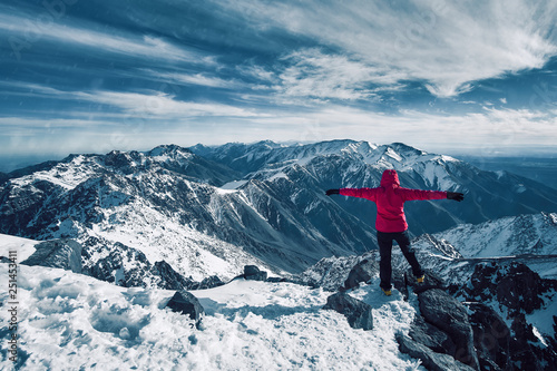 Happy alpinist girl standing at snow covered top of the peak of Jebel Toubkal in Atlas mountains Morocco